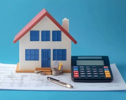 Small model home next to a calculator and pen. Concept for mortgage payment calculator